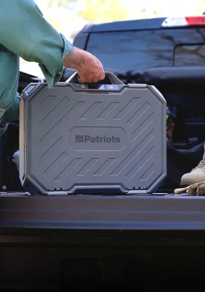 A person’s hand lifting a large, rugged grey 4Patriots AlphaCase portable power station from the bed of a black pickup truck.