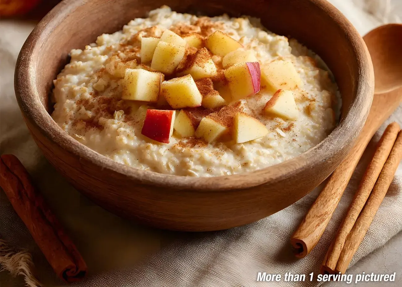 Apple Cinnamon Cream of Wheat Pouch A rustic wooden bowl filled with creamy Cinnamon Cream Wheat cereal, topped with diced red apples and a dusting of cinnamon powder, set against a warm background with cinnamon sticks.