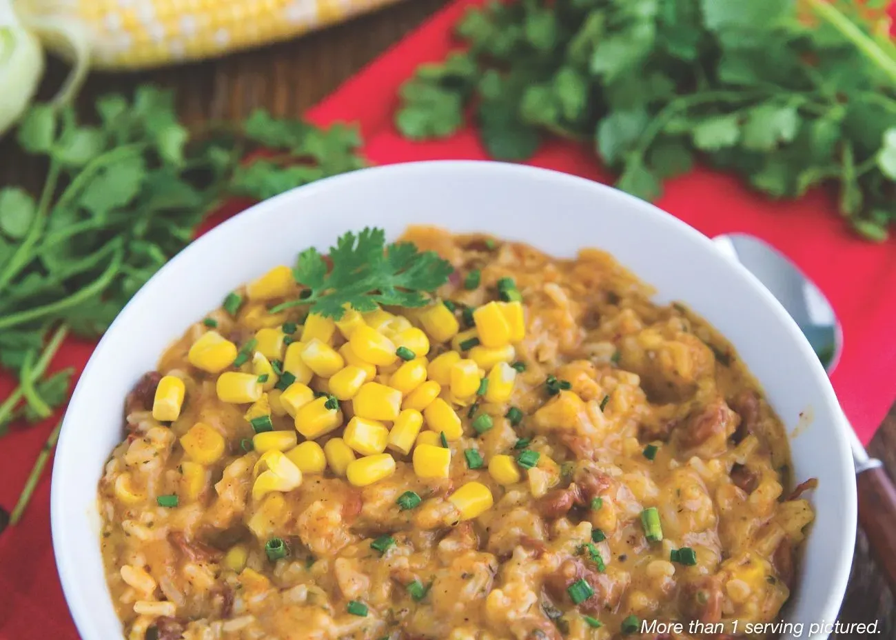 Cowboy Rice & Beans Emergency Supply A white bowl filled with a hearty mix of rice and beans, topped with sweet corn kernels and fresh cilantro, set against a vibrant red background.