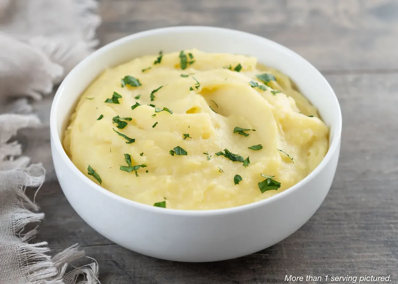 Creamy Herbed Mashed Potoates Emergency Supply Food Kit A simple white bowl filled with smooth, fluffy mashed potatoes topped with fresh chopped green herbs, set against a rustic wooden background.
