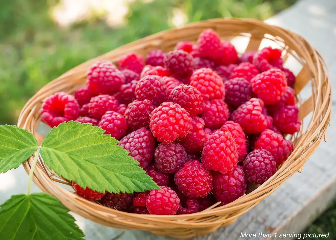 Freeze-Dried Raspberries Emergency Supply Food Kit A small wicker basket overflowing with vibrant red raspberries, shown with a fresh green leaf on top.