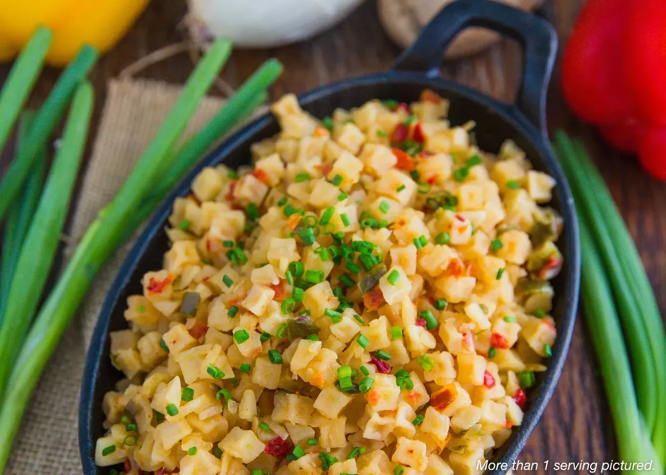 Potatoes O'Brien A black cast-iron skillet filled with diced potatoes, red and green peppers, and onions, garnished with fresh chives and surrounded by whole peppers and green onions.