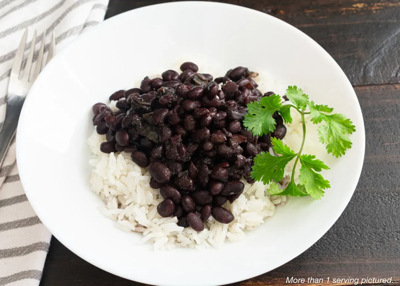 A white bowl featuring a heap of seasoned black beans served over a bed of fluffy white rice, garnished with a fresh cilantro sprig.