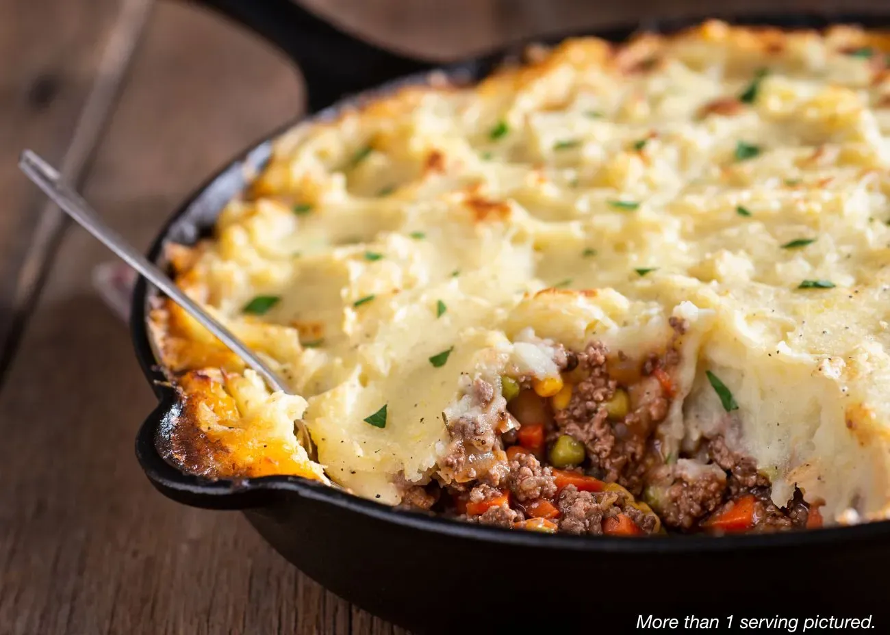 Shepard's Pie A black cast-iron skillet filled with Shepard's Pie, featuring a layer of savory ground meat and vegetables topped with a thick, golden-brown crust of mashed potatoes garnished with parsley.
