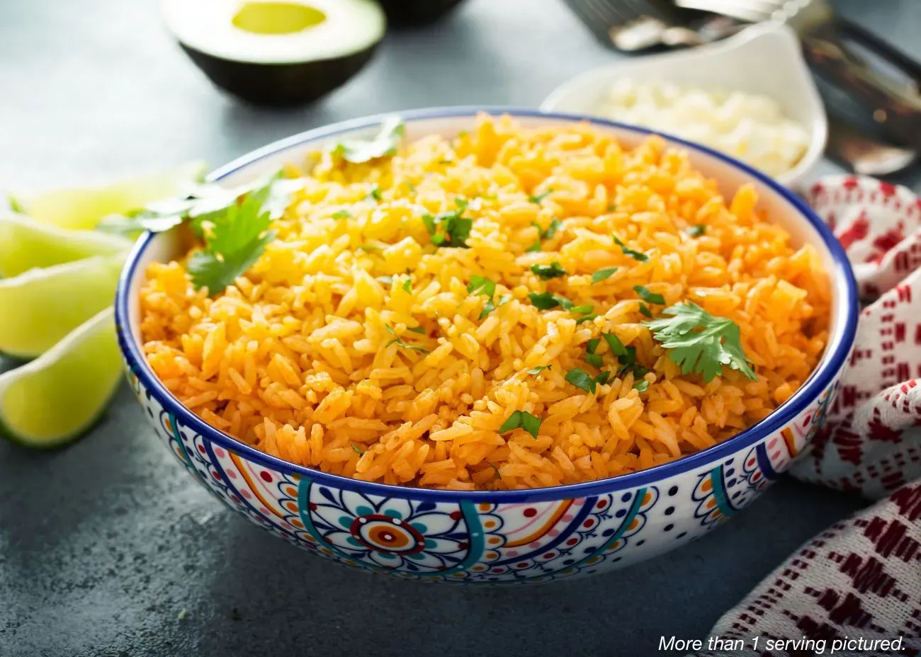 4-Week Emergency Supply Food Kit Frank's Favorite Alfredo A decorative blue and white bowl filled with savory Spanish Rice garnished with fresh cilantro, served with lime wedges, avocado, and a small side of white cheese.