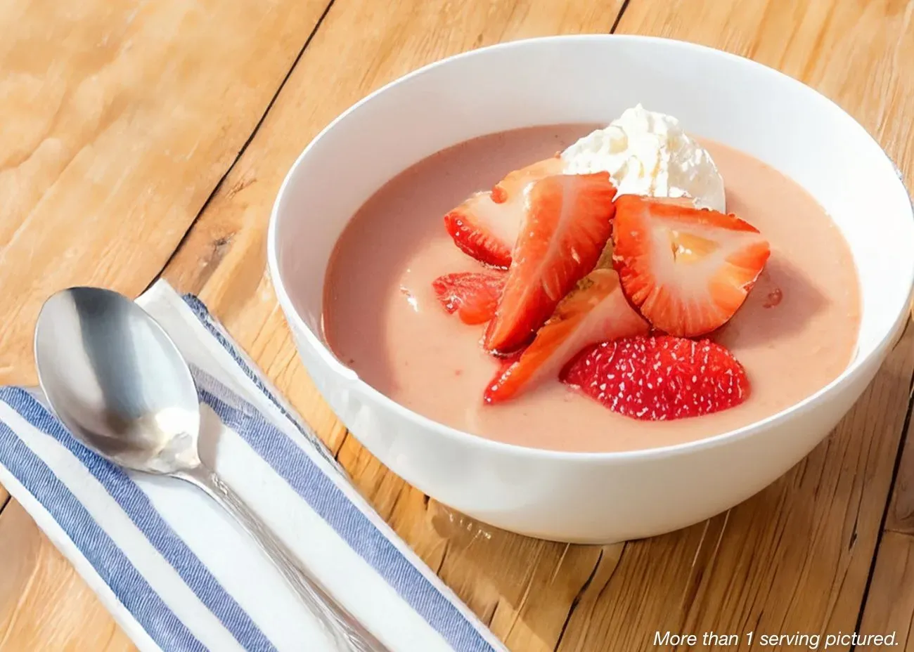 Strawberries & Cream Pudding A smooth, pink strawberry cream dish in a white bowl, topped with fresh strawberry slices and a dollop of whipped cream, served on a light wooden surface.