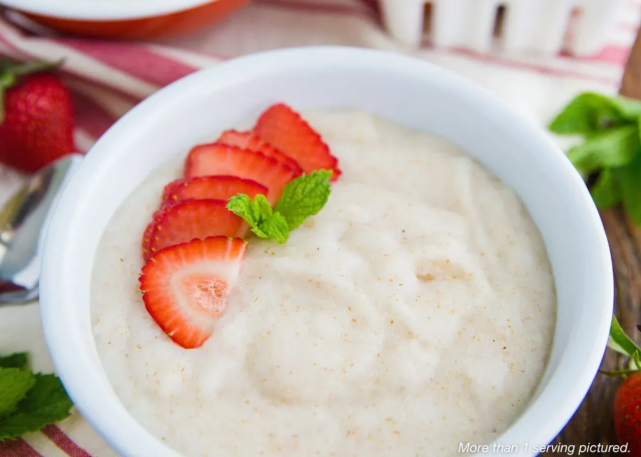 Sweetberry Creamy Wheat A white bowl of creamy hot wheat cereal topped with a row of fresh strawberry slices and a small mint leaf garnish.