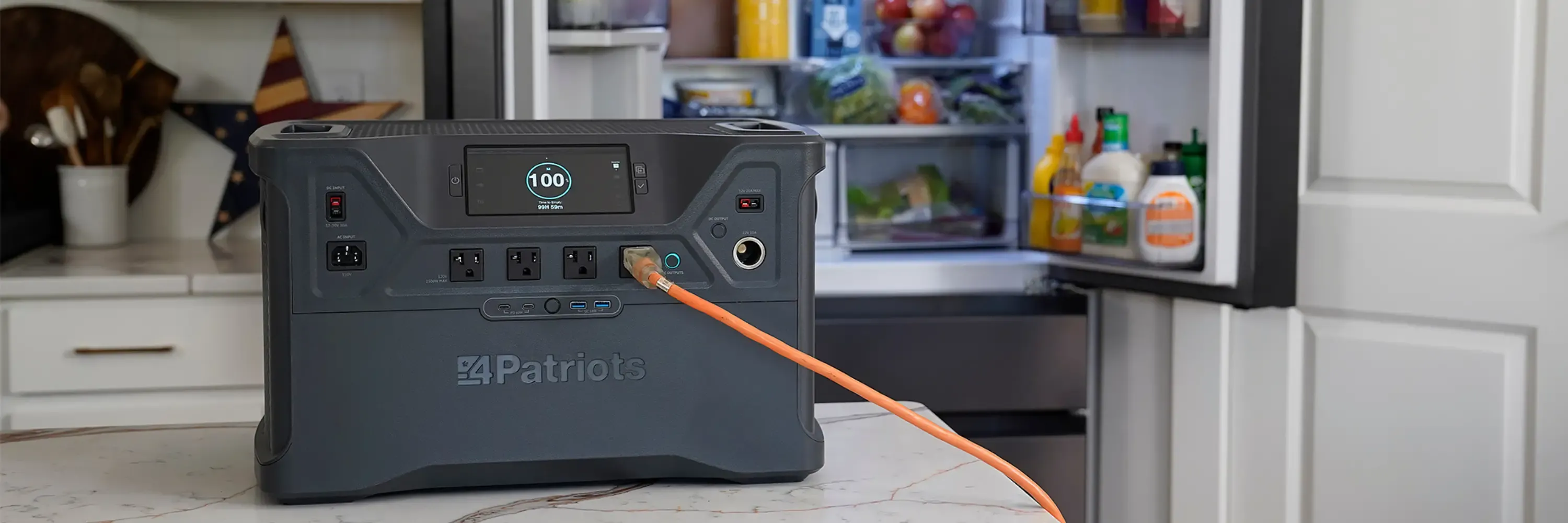 Patriot Power Solar Generator 2500X powers fridge A 4Patriots portable power station sits on a kitchen counter with an orange power cord plugged into it, supplying backup power to an open refrigerator stocked with groceries. The digital display on the power station shows a full 100% charge, emphasizing its emergency preparedness role.