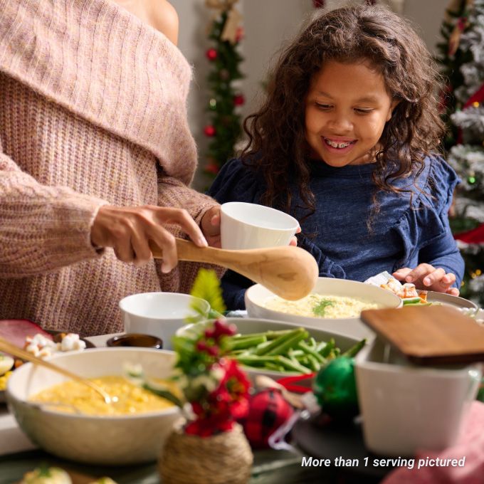 A mother fills her daughter's plate with creamed corn for Christmas dinner.