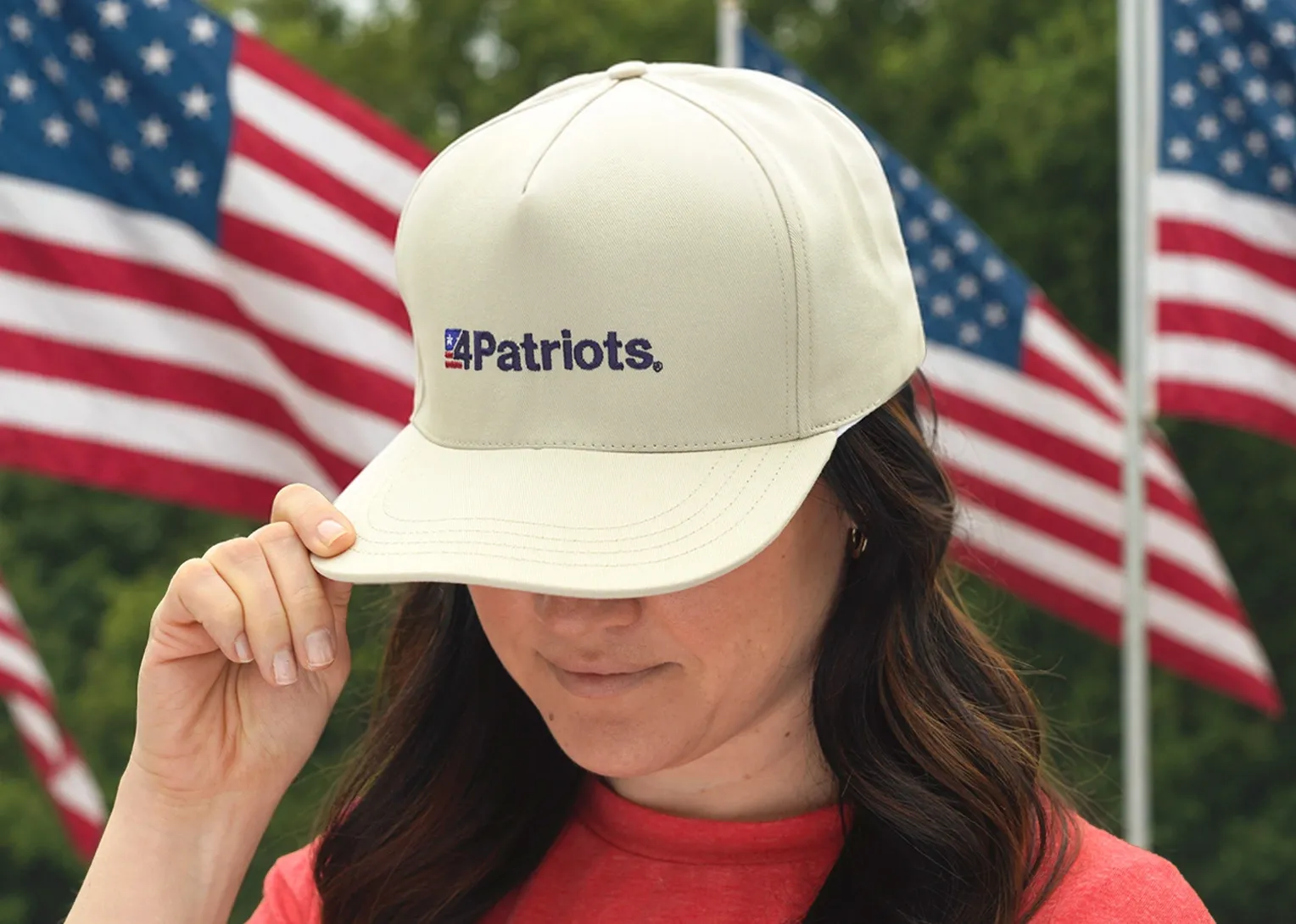 A smiling woman stands behind a table displaying a 4Patriots Patriot Power Solar Generator 2200X and folded 200-Watt solar panel and a Patriot Power Sidekick Solar Generator and foldable 40-Watt solar panel decorated with American flags, patriotic balloons and bunting at an outdoor backyard gathering during sunset.
