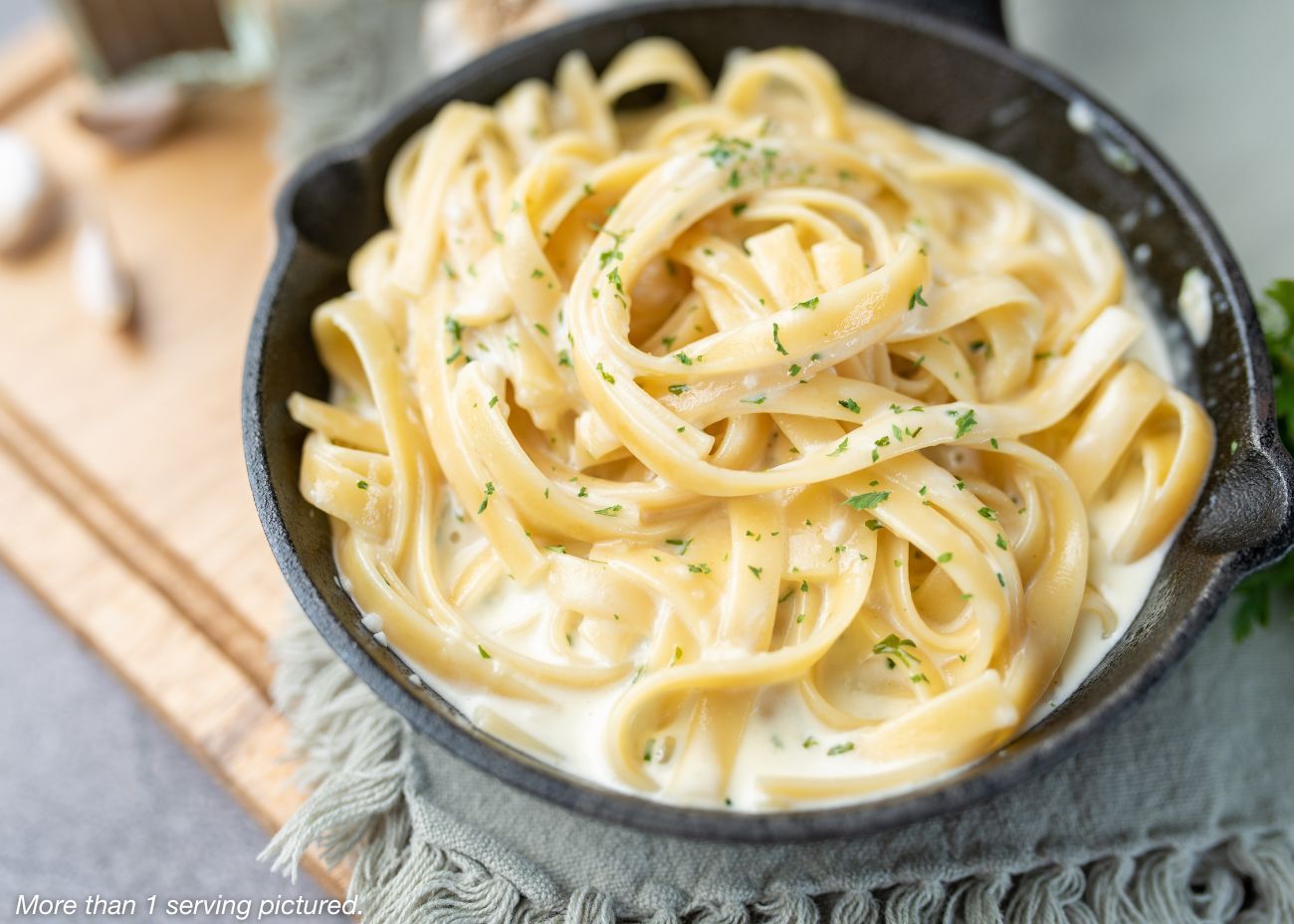 A bag of 4Patriots Dinner Bell Broccoli Bake meal sits on a white wooden surface surrounded by a block of cheddar cheese, fresh broccoli, and a cheesy baked broccoli casserole. The packaging emphasizes quick preparation and satisfaction guaranteed.