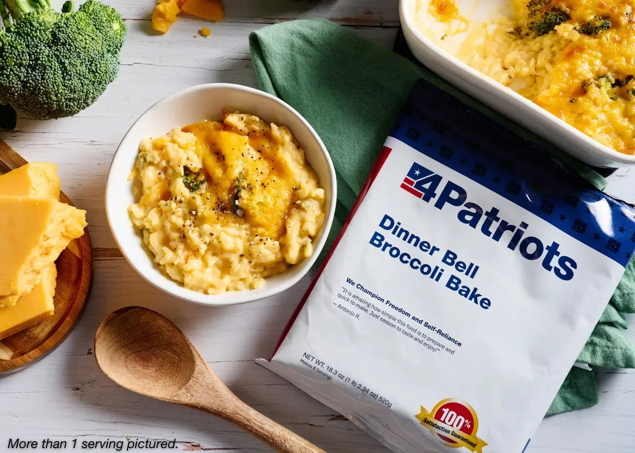 A bag of 4Patriots Dinner Bell Broccoli Bake meal sits on a white wooden surface surrounded by a block of cheddar cheese, fresh broccoli, and a cheesy baked broccoli casserole. The packaging emphasizes quick preparation and satisfaction guaranteed.