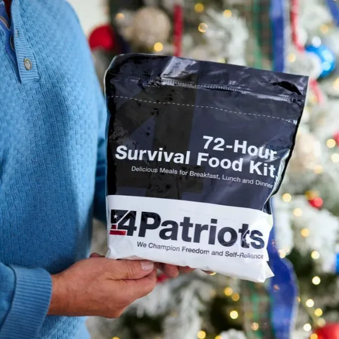 A person in a blue sweater holding a black and white 4Patriots 72-Hour Survival Food Kit in front of a decorated Christmas tree.