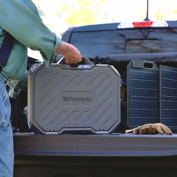 Person loads a 4Patriots Patriot Power Generator AlphaCase Elite next to solar panel in a truck bed.