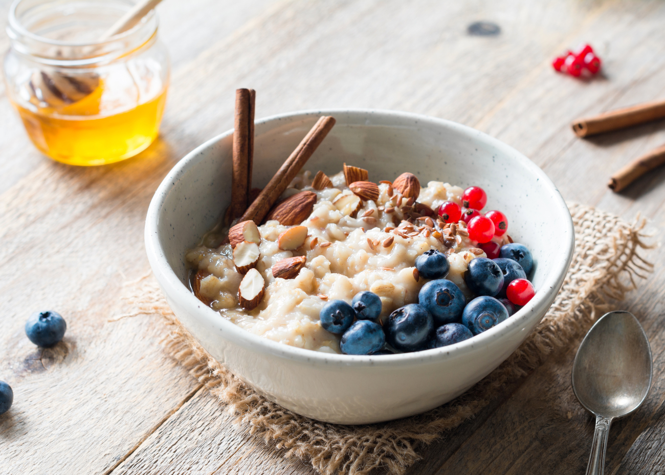 A bag of 4Patriots Dinner Bell Broccoli Bake meal sits on a white wooden surface surrounded by a block of cheddar cheese, fresh broccoli, and a cheesy baked broccoli casserole. The packaging emphasizes quick preparation and satisfaction guaranteed.