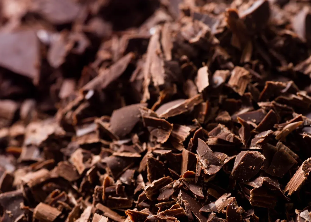 A close-up of finely chopped dark chocolate pieces, showing their rich brown color and textured, flaky surface.