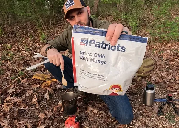 A man holding a package of 4Patriots Aztec Chili with Mango survival food in the woods.