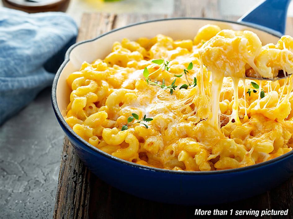 The image features a skillet of America's Finest Mac & Cheese. In the background is a casual table setting. More than 1 serving pictured.