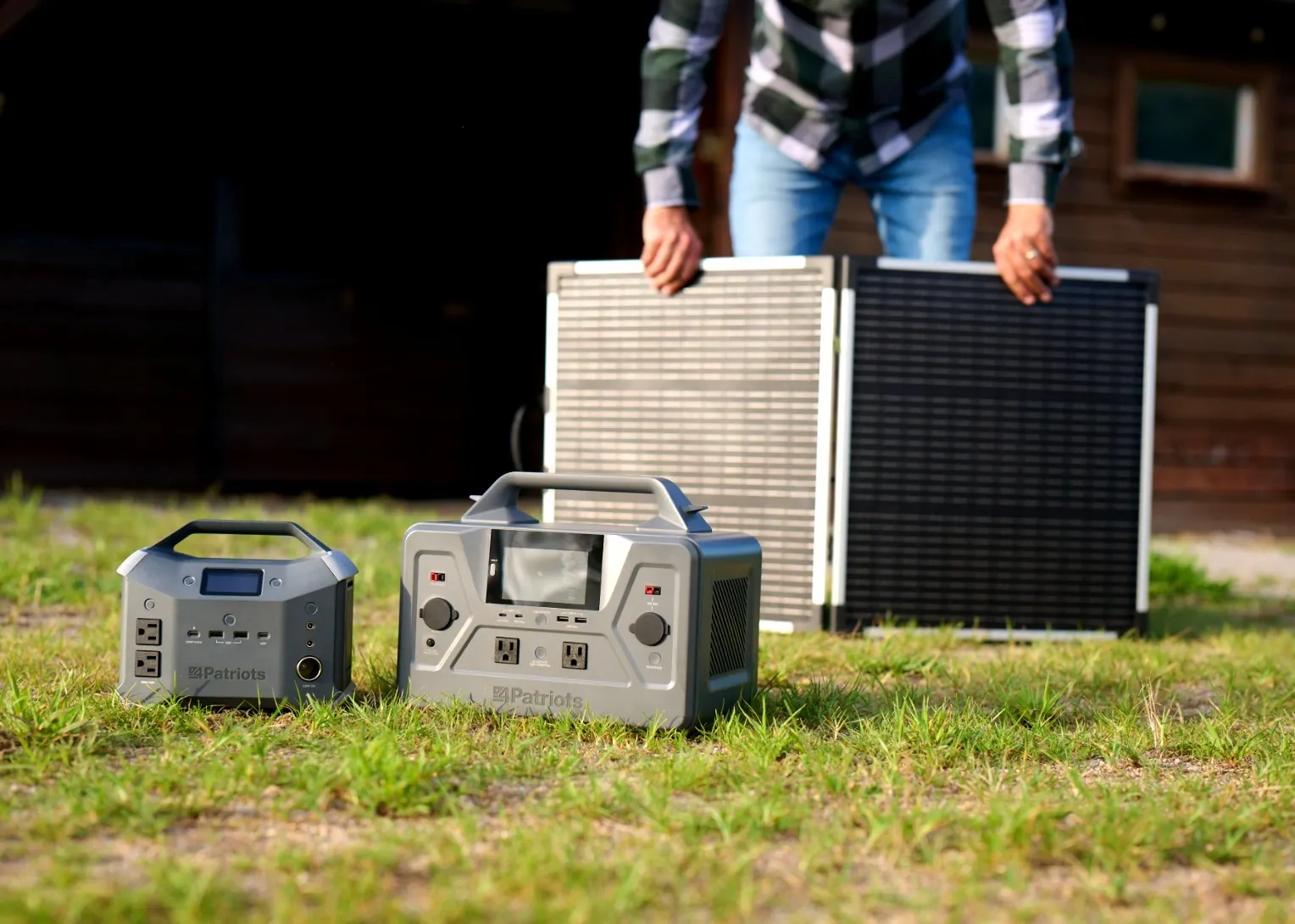 Compact and full-size 4Patriots portable power stations on grass beside a foldable 100-Watt solar panel for off-grid backup power